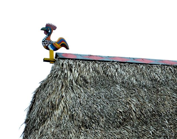 A replica of a rooster on the roof of a stilt house