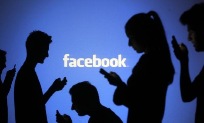 People are silhouetted as they pose with mobile devices in front of a screen projected with a Facebook logo. Photo by Reuters 