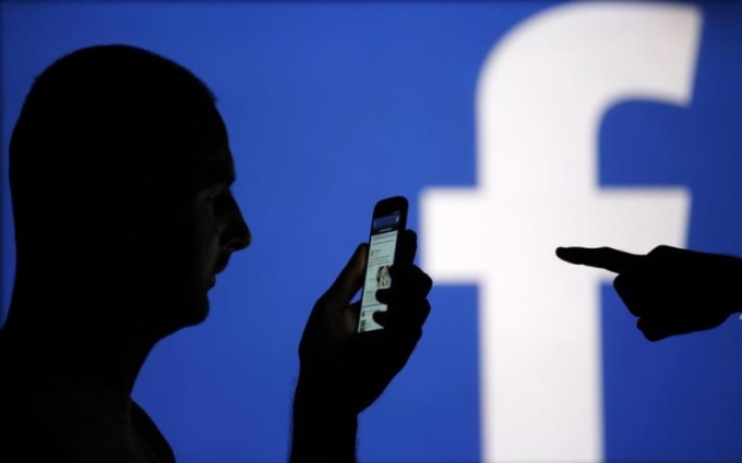 A man is silhouetted against a video screen with a Facebook logo. Photo by Reuters/Dado Ruvic 