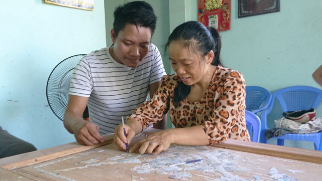 Nguyễn Huy Hoàng đang hướng dẫn thợ trong phân xưởng của mình các thao tác chạm khảm trên gỗ. Ảnh: H.L