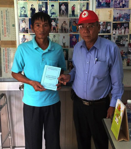 Ông Nguyễn Tam Chiến (phải), Chủ tịch Hội Chữ thập đỏ phường Hòa Cường Bắc trao sổ nhận gạo hằng tháng cho hộ nghèo.