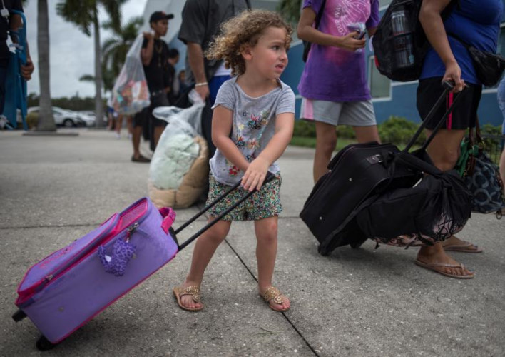 Bé Chloe Rosenberger, 3 tuổi ở Cape Coral, Florida kéo chiếc vali chứa đồ đạc đi theo anh trai và mẹ đến nơi trú ẩn tạm thời ở Estero. Ảnh: Reuters.