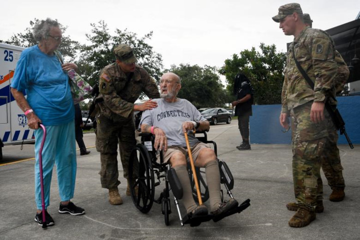 Binh sĩ của lực lượng Vệ binh Quốc gia thuộc tiểu Đoàn 2, Trung Đoàn Bộ Binh 124 trợ giúp một cặp vợ chồng già bên ngoài trung tâm tạm trú Germain ở Estero.