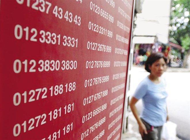 A woman walks past a board showing telephone numbers on sale (Photo: laodong.vn)