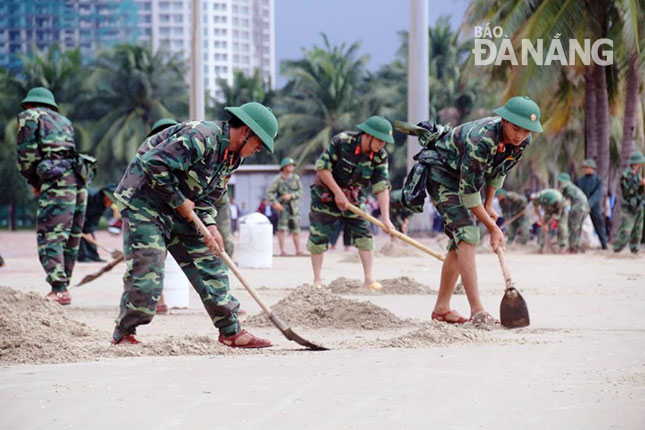 Trên bờ biển, lực lượng quân đội khẩn trương cào cát, bảo đảm mặt bằng sạch, đẹp cho Công viên Biển Đông.  Ảnh: THANH TÌNH