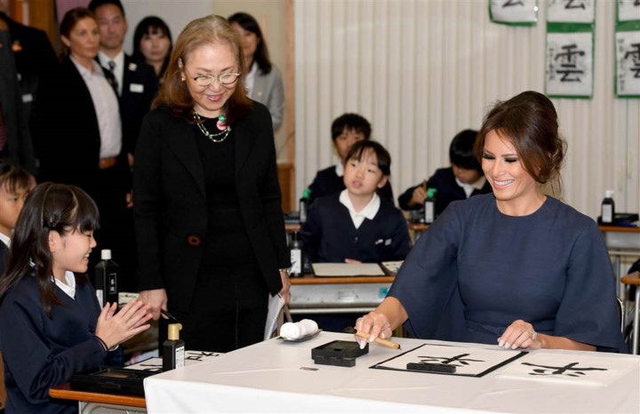   Bà Melania Trump viết thư pháp với sự hỗ trợ của một nữ học sinh. Bà đang có mặt tại lớp thư pháp cùng với bà Akie Abe, vợ của Thủ tướng Abe. Ảnh: EPA.
