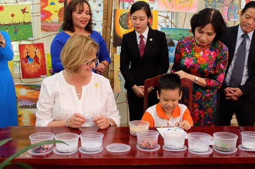 Ms Nancy Lange de Kuczynski eagerly learning about how to thread beads with a thin string to make bracelets at the Centre (Photo: http://apec2017.danang.gov.vn )