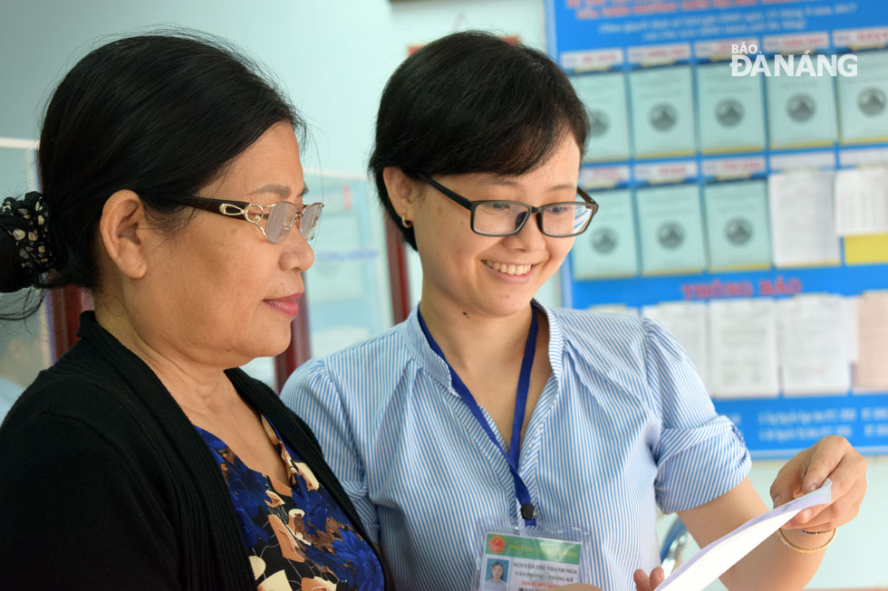 A female employee from Son Tra District’s An Hai Dong Ward People’s Committee (PC) (right) introducing insurance claims process for a local resident.