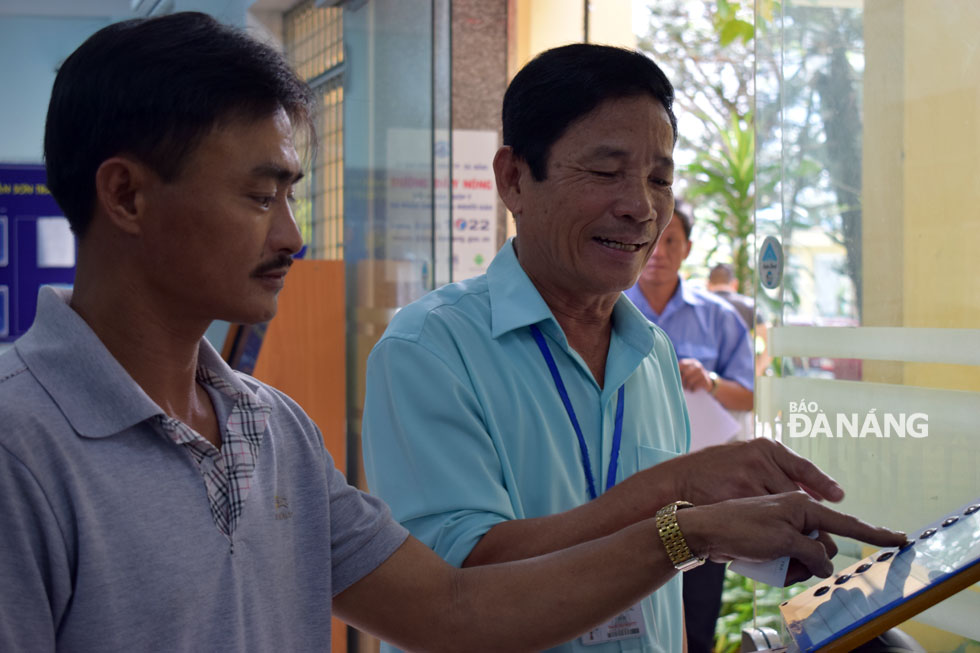 An employee from the Son Tra District PC (right) instructing a citizen how to use an automatic queuing machine