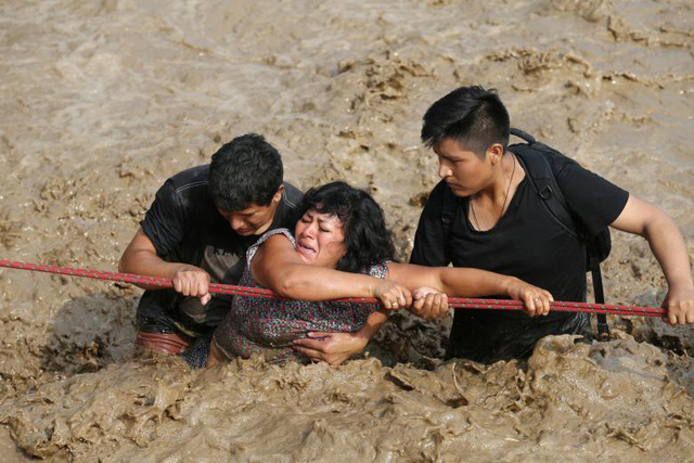 Những người dân ở Huachipa, Peru bám vào sợi dây để vượt qua đoạn đường bị lũ quét khi sông Huaycoloro vỡ bờ hôm 17/3.