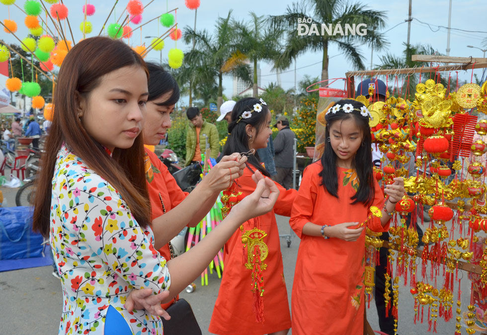 Young women in ‘Ao Dai’ buying red envelopes and Tet decorative hanging items