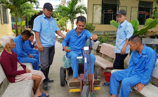 Ông Ngô Văn Dũng (giữa) được nhân viên Trung tâm BTXH Đà Nẵng hướng dẫn đi bằng xe tay quay phục hồi chức năng. Ảnh: V.T.L