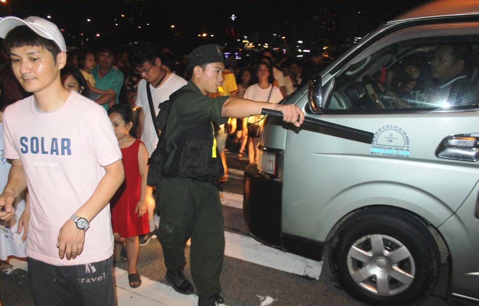 Một chiến sĩ cảnh sát cơ động nhoài người chặn xe để bảo đảm an toàn cho một đoàn khách xem pháo hoa đang đi qua đường.  Ảnh: Hoàng Hiệp.
