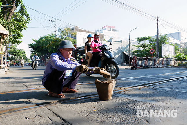 Bất chấp hiểm nguy từ phương tiện qua đường, anh Cường làm vệ sinh đường ray để đoàn tàu đi qua được thông suốt. Ảnh: PHAN CHUNG