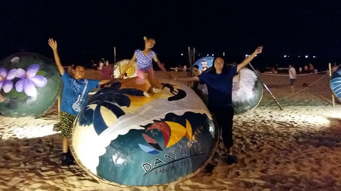 Tourists snap a photo with a coracle with painting on beach of Đà Nẵng. — VNS Photo Công Thành Read more at http://vietnamnews.vn/life-style/449158/my-khe-beach-to-host-summer-week.html#Xvf8GatK5LAItBC2.99