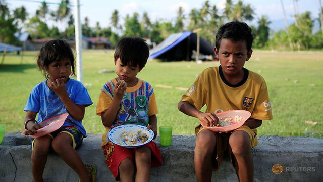Trẻ em ngồi ăn bên ngoài lều dựng tạm cho những người sơ tán sau động đất/sóng thần ở Indonesia. (Ảnh: Reuters)