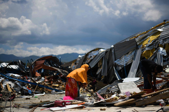 Một phụ nữ cố tìm kiếm những đồ còn dùng được từ đống đổ nát sau thảm họa. (Ảnh: AFP)
