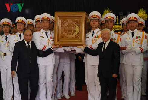 Tổng Bí thư Nguyễn Phú Trọng và Thủ tướng Nguyễn Xuân Phúc đứng hai bên cùng nâng linh cữu đồng chí Đỗ Mười đang di chuyển ra cỗ linh xa.