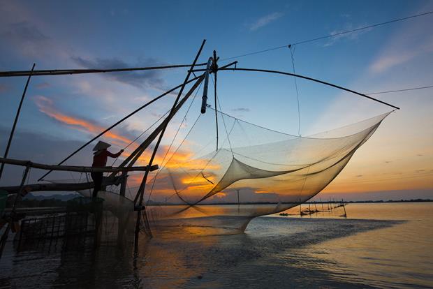 A shore-operated stationary lift net is dropped in the water at sunset