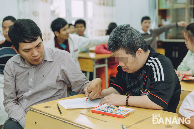 Thầy Trương Tấn Dũng đang hướng dẫn một em học sinh tập tô màu. Ảnh: HÀ TIẾN ANH