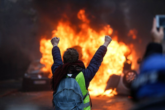 Một người biểu tình đứng trước xe ô tô bị đốt tại Paris hôm 1/12. (Ảnh: AFP)