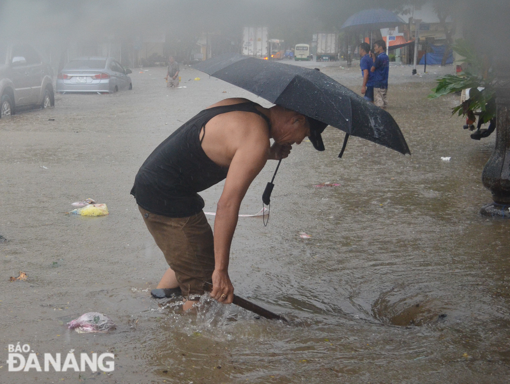 Một người dân đội mưa để khơi cống thoát nước trên đường Tú Mỡ, khu vực sau lưng Bến xe trung tâm. Ảnh: XUÂN SƠN