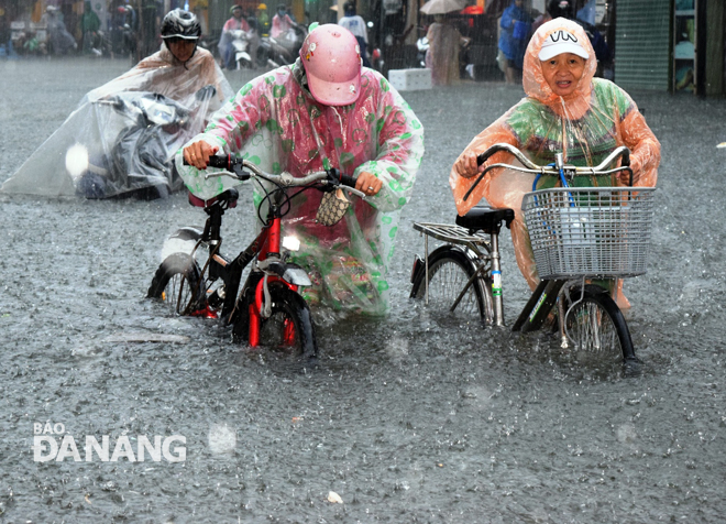 Road users pushing their vehicles through an inundated street