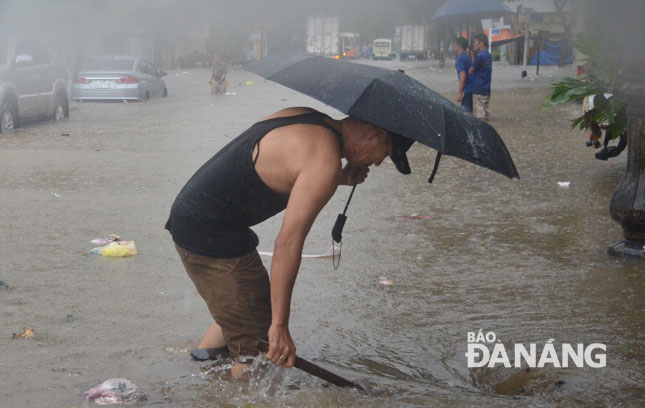 Một người dân đội mưa để khơi cống thoát nước trên đường Tú Mỡ, khu vực sau lưng Bến xe Trung tâm. 					                     Ảnh: XUÂN SƠN