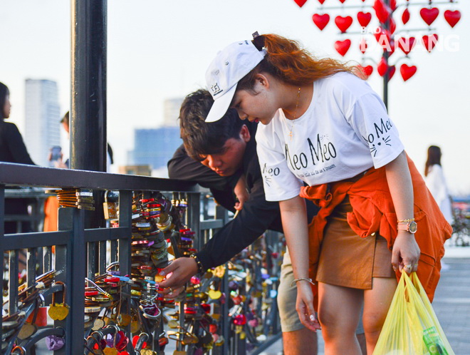 A couple hanging a love padlock on the steel bar of the bridge.