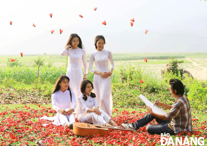 Under the shadow of a large Bombax ceiba tree, group of young people are interested in taking souvenir photos with red flowers whose petals are falling down onto the ground