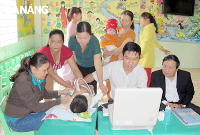 Chị Trần Thị Trinh (trái) trong một lần hỗ trợ các bác sĩ khám sàng lọc tim miễn phí cho trẻ sơ sinh trên địa bàn huyện Hòa Vang.