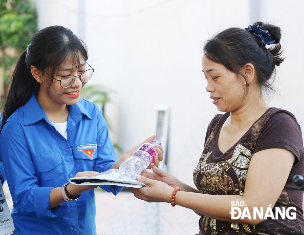 A volunteer giving a water bottle and newspaper to a middle-aged woman who was waiting for an exam candidate