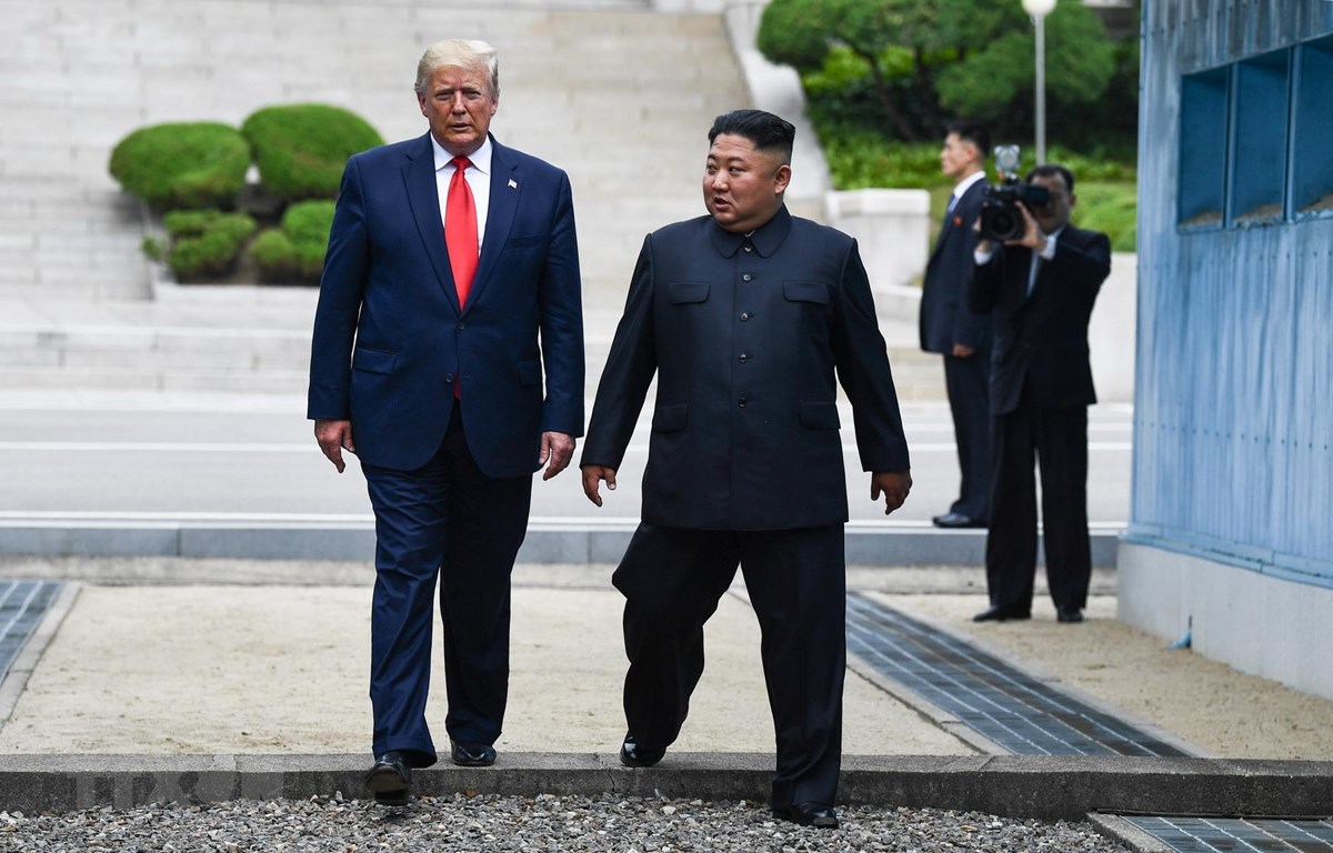 Tổng thống Mỹ Donald Trump (trái) và nhà lãnh đạo Triều Tiên Kim Jong-un bước chân qua đường ranh giới phân chia hai miền Triều Tiên tại DMZ, sang phần lãnh thổ của Triều Tiên. (Ảnh: AFP/TTXVN)