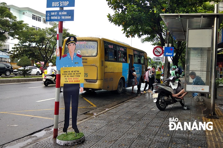 A life-size dummy traffic inspector standing at a bus stop in front of C17 Military Hospital on Nguyen Huu Tho Street