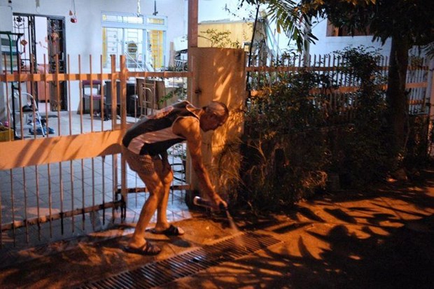 A resident of Hemsley Avenue in Singapore sprays insecticide outside his house (Photo: Strait Times)