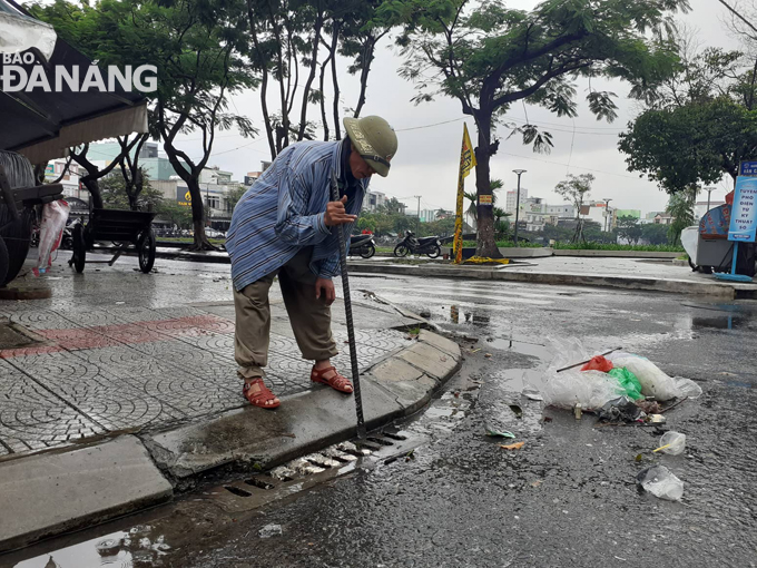 Một người dân sinh sống tại đường Hàm Nghi đã tự giác thu gom rác, khơi thông cống thu nước để giảm ngập trên đường phố. Ảnh: Hoàng Hiệp