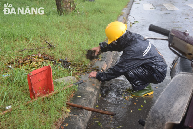 Một công nhân Xí nghiệp Môi trường Sơn Trà thu nhặt lá cây ở một cửa thu nước mưa để bảo đảm thoát nước cho đường Trần Hưng Đạo