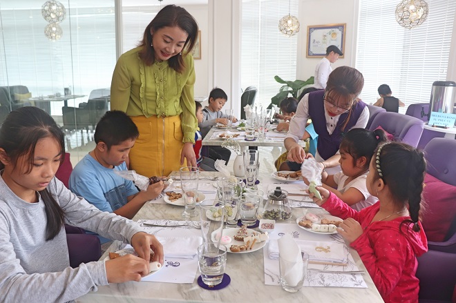 Bà Wen Yi Chun (áo xanh) và nhân viên nhà hàng hướng dẫn các em cách làm bánh.