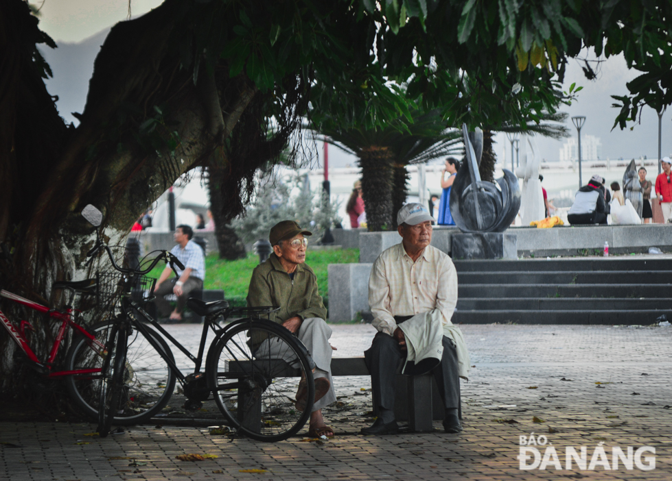 Senior citizens sitting on a public bench on the pavement of Bach Dang Street