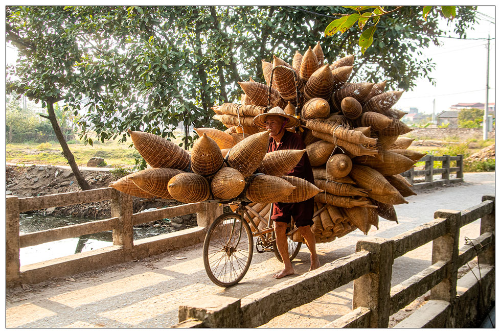 An artisan walking with his bicycle hanging bamboo fish traps 