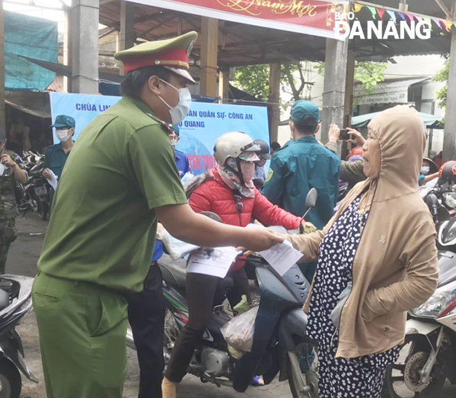 Lực lượng Công an phường phát khẩu trang miễn phí cho người dân, tiểu thương tại chợ Mai. Ảnh: NGỌC PHÚ