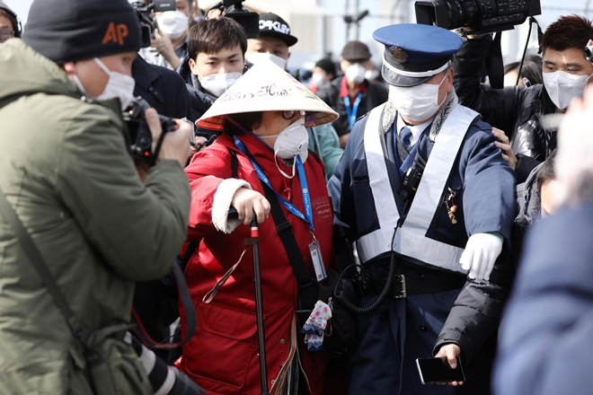 Cảnh sát hộ tống một nữ hành khách khỏi vòng vây của báo giới sau khi rời du thuyền Diamond Princess.Ảnh: Reuters