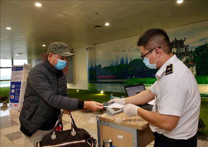 Nhân viên y tế kiểm tra phiếu khai báo y tế của hành khách trước khi làm thủ tục nhập cảnh tại cửa khẩu Sân bay quốc tế Nội Bài (Hà Nội), chiều 7/3. Ảnh: Dương Giang/TTXVN