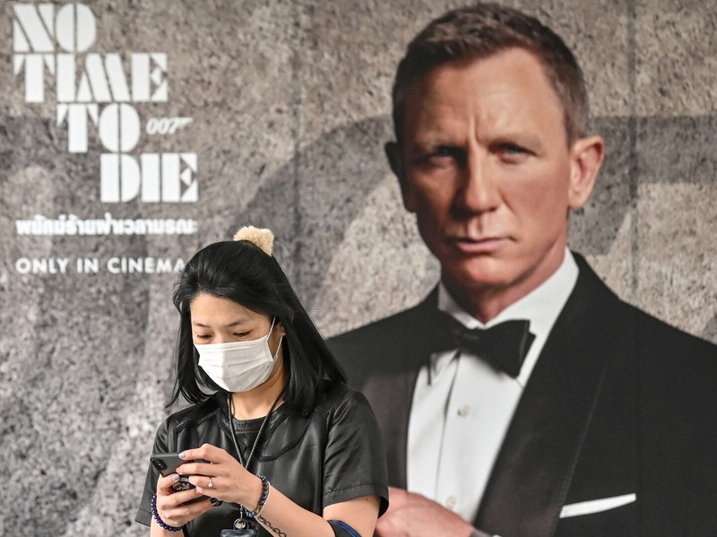 Một cô gái đeo khẩu trang, đứng trước poster quảng bá bộ phim James Bond 