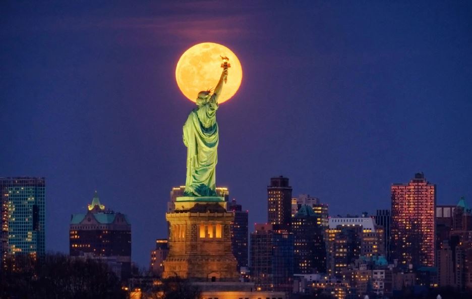 Trăng tròn tháng 3 xuất hiện đằng sau tượng Nữ Thần tự do ở New York, Mỹ. Ảnh: AP