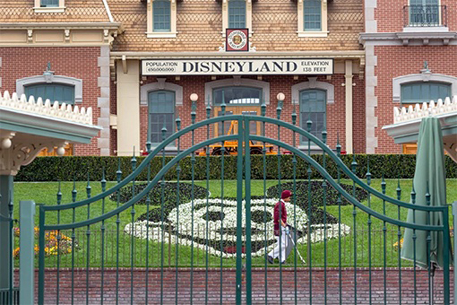 Một nhân viên dọn dẹp khu đất phía sau cánh cổng đóng kín của Công viên Disneyland và Disney California Adventure vào ngày 14 -3.