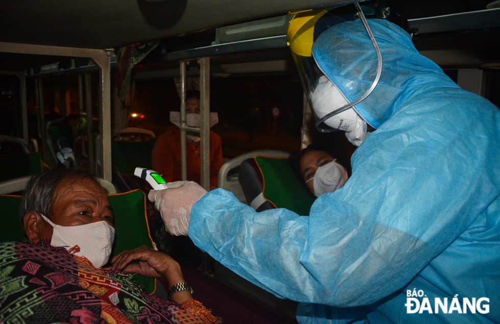 A medical worker checking the temperatures of bus passengers at the Hoa Phuoc entrance gate in Hoa Vang District in the early morning of 18 March