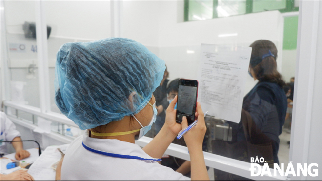 Nhân viên y tế Bệnh viện Đà Nẵng tiếp nhận thông tin bệnh nhân nghi nhiễm SARS-CoV-2 để khám, thông qua lớp kính cách ly. 										Ảnh: PHAN CHUNG