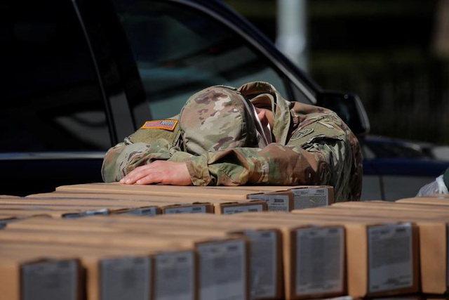 Một thành viên lực lượng vệ binh quốc gia Mỹ ngủ gục trên các thùng chứa đồ ăn phân phát cho người dân ở Manhattan, New York hôm 1-4. (Ảnh: Reuters)