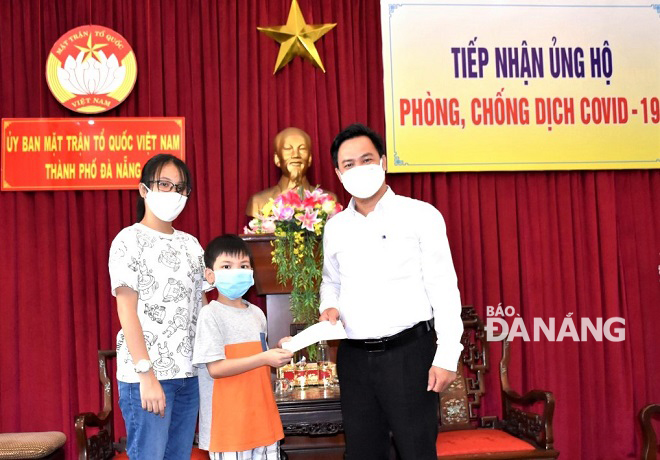 Chánh văn phòng Ủy ban MTTQ Việt Nam thành phố Phạm Phú Bình (bìa phải) tiếp nhận tiền ủng hộ từ cháu Bùi Hồng Kiên (giữa). Ảnh: TT